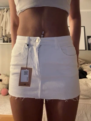 Vit jeanskjol med rå kant - Säljer en vit kort jeanskjol med rå, fransig kant och klassiska fem fickor som är för liten för mig. Kjolen har bälteshällor och stängs med knapp och dragkedja framtill. Perfekt för dig som gillar en clean och enkel stil.🥰