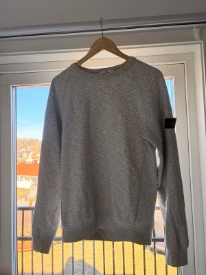Grå sweatshirt från Stone Island - Säljer en stilren grå sweatshirt från Stone Island med klassisk rund hals och den ikoniska loggan på vänster ärm. Tröjan har en avslappnad passform och är tillverkad i mjukt bomullsmaterial. Perfekt för en casual look. Säljer den eftersom den inte kommer till användning så ofta. Sjukt snygg och bra skick! Tveka inte på att ställa frågor om du har några! Storleken är som en M tröja🤩😁