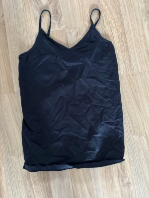 Svart linnetopp med smala axelband - En enkel och stilren svart linnetopp med smala axelband och v-ringad hals. Perfekt att matcha med jeans eller kjol för en clean look. Tunn och lätt, passar bra till varma dagar eller träning.