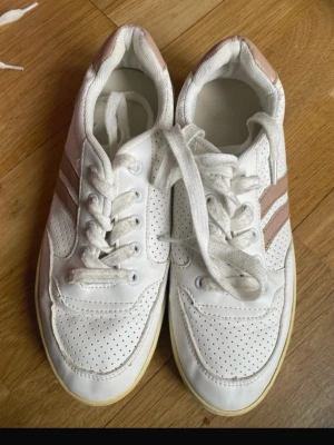 Vita sneakers - Snygga vita sneakers med perforerat mönster och två ljusbruna ränder på sidan. Skorna har klassisk låg modell, det fattas innersulorna kan köpas överallt 