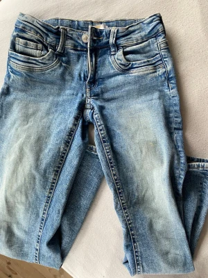 Blå Low waist jeans  - Säljer ett par blå jeans med snyggt slitna detaljer och klassisk femficksdesign. Jeansen har normal midja, raka ben och är gjorda i denim med ljus tvätt. Perfekta för dig som gillar en avslappnad och trendig look.