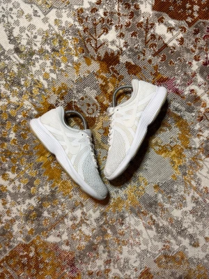 Vita mesh sneakers från Nike - Snygga vita sneakers från Nike med ovandel i mesh och syntetiska detaljer. Skorna har en låg profil, klassisk snörning och en bekväm, dämpad sula med mönstrad undersida. Perfekta för en clean och sportig look.