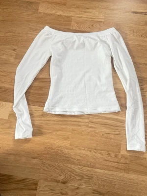 Vit offshoulder långärmad topp - Snygg vit offshoulder topp med långa ärmar. Enkel och stilren design som passar perfekt till jeans eller kjol. Tillverkad i mjukt bomullsmaterial för en bekväm känsla och smickrande passform.