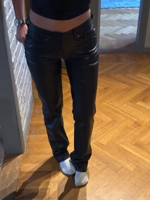 Svarta skinnbyxor med raka ben - Snygga svarta skinnbyxor med raka ben och klassisk femficksmodell. Byxorna har normal midja och stilrena sömmar både fram och bak. Perfekta för dig som vill ha en edgy och trendig look.