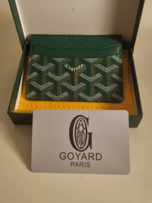 Grön korthållare från Go4yard - Snygg grön korthållare från Go4yard med det klassiska vita och gröna Go4yard-mönstret. Tillverkad i canvas och läder, har flera fack för kort och detaljer i guldtext. Perfekt för dig som vill ha något både stilrent och exklusivt.