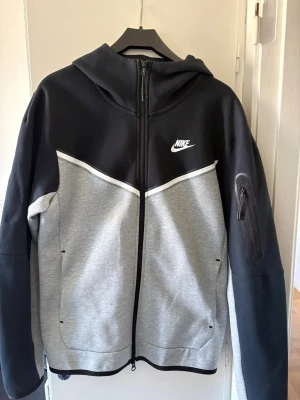 Grå svart Nike tech fleece  - Snygg zip up hoodie från Nike i modellen Nike tech fleece. Har drag kedja på armen samt en lång på bröstet. Tröjan är använd en tal gånger. Inga märken eller skador skriv för mer frågor!