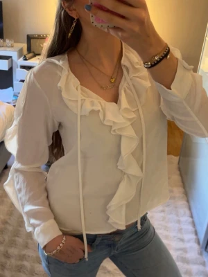 Vit blus från Zara med volang och knytband - Snygg vit blus från Zara med långa ärmar med volanger och volanger längs urringningen. Har en pytteliten fläck, se bild 5