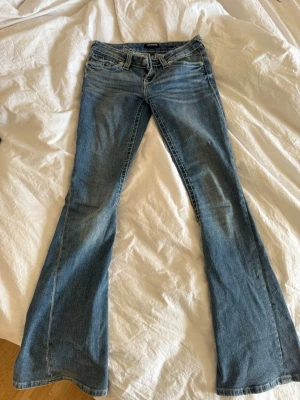 Blå bootcut jeans från True Religion - Säljer ett par blå bootcut jeans från True Religion med snygga slitningar och kontrastsömmar. Klassisk femficksmodell och låg midja. Jeansen har en cool broderad detalj på insidan av linningen och är tillverkade i mjuk denim.