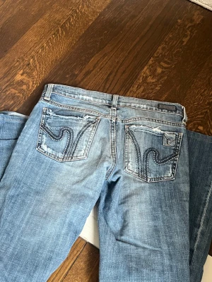 Citizens of humanity bootcut jeans   - Säljer ett par blå jeans från citizens of humanity med slitningar och hål på framsidan. Jeansen har snygga broderade bakfickor med vågigt mönster och klassisk femficksdesign. Perfekt för dig som gillar en cool och avslappnad stil.