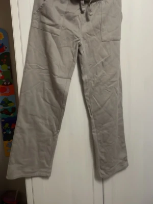 Beiga mjukisbyxor med raka ben - Säljer ett par gråa mjukisbyxor med raka ben och resår i midjan. Byxorna har stora fickor både fram och bak samt dragsko i midjan för extra komfort. Dem är perfekta om man gillar att vika ner midjebandet på byxorna.