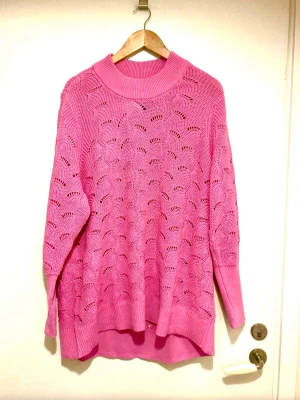 Oversized rosa stickad tröja - Säljer en oversized stickad tröja i stark rosa färg med hålmönster och bred ribbad krage. Tröjan har långa ärmar och ribbade muddar vid ärmslut och nederkant. Perfekt för dig som gillar färg och vill ha en mysig look.