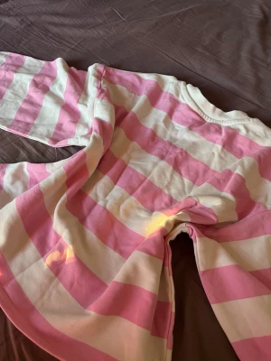 Rosa och vit randig croppad topp - Superfin croppad långärmad topp med breda rosa och vita ränder. Tröjan har en relaxed fit och ribbade muddar vid ärmslut och halsringning. Perfekt för en chill och trendig look. 152 cm