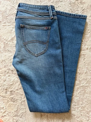 Blå raka jeans från Tommy Hilfigher - Snygga blå jeans med klassisk rak passform och fem fickor. Jeansen har en medelhög midja och subtila slitningar framtill för en trendig look. 
