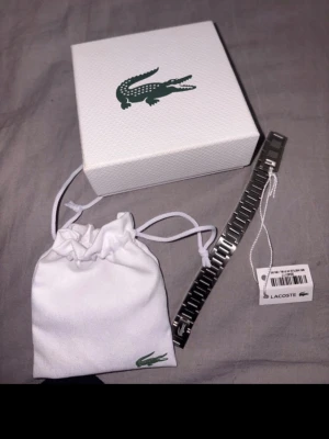 Silverfärgad klocka från Lacoste - Stilren klocka från Lacoste i silverfärgat metallarmband. Kommer med originalförpackning och tygpåse med Lacoste-logga. Perfekt accessoar för dig som gillar klassisk och sportig stil.