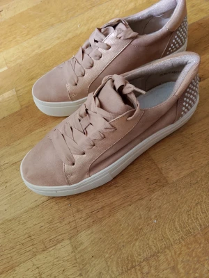 Ljusrosa sneakers med vita pärl detaljer - Snygga ljusrosa sneakers med breda matchande skosnören och vit sula. Baksidan är dekorerad med vita pärl prickar för en extra touch. Skorna har en klassisk låg modell och är tillverkade i ett mjukt tygmaterial.  Kostat 399kr,prislappen sitter kvar under skon,skorna är Storlek 39