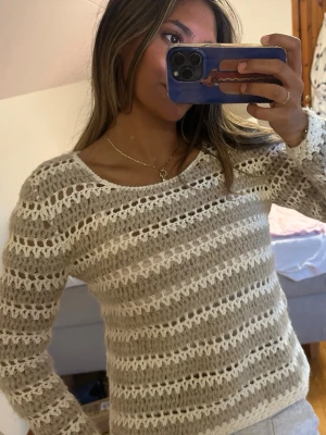 Beige och vit stickad tröja - Säljer en stickad tröja i beige och vitt med genombrutet mönster och långa ärmar från Massimo Dutti.  Tröjan har rund halsringning och är gjord i ett mjukt, luftigt garn som värmer. OBS har rosa linne under