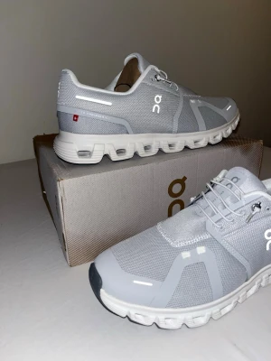 Grå sneakers från On med vit sula - Snygga grå sneakers från On med vit, unik sula och diskreta reflexdetaljer. Skorna har mesh-yttermaterial och klassisk snörning. Perfekta för dig som gillar stilren och sportig design.