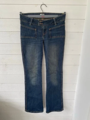 Blå bootcut jeans från 157 - Snygga blå bootcut jeans från 157 med dubbla knappar i midjan och stora framfickor. Jeansen har klassisk femficksdesign, markerade sömmar och lätt slitning på låren. Storlek: xs Längd: lång