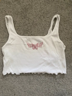 Vit croppad linnetopp med fjäril - Söt vit croppad linnetopp med rosa fjärilsmotiv framtill. Säljer då de tyvärr inte passa mig 