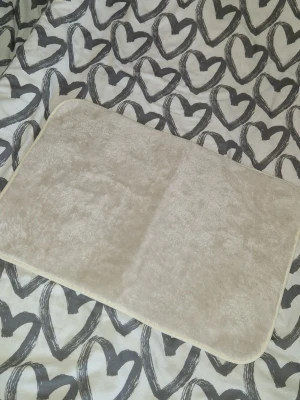 Badrumsmatta - En enkel och stilren mjuk beige badrumsmatta med mjuk, fluffig yta. Rektangulär form och rundade hörn, perfekt som liten matta till badrum, hall eller vid sängen. Materialet känns lent och bekvämt under fötterna. Ca 40×60cm