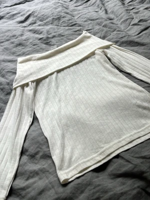 Vit offshoulder topp med ribbade ärmar - Snygg vit offshoulder topp med långa, ribbade ärmar och diskret randigt mönster. Perfekt för dig som gillar en stilren och trendig look. Mjuk och skön i materialet, passar till många outfits.