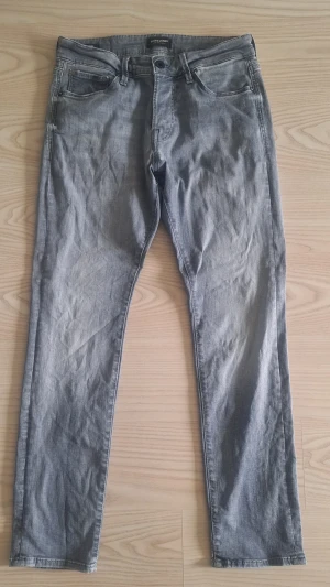 Grå slim fit jeans Jack & Jones i nyskick W29 L30 - Snygga grå slim fit jeans från Jack & Jones, modell Glenn, med klassisk femficksdesign och dragkedjegylf. Jeansen har en ljus tvätt och raka ben, perfekta för en avslappnad och trendig look.