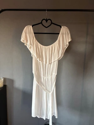 Vit off shoulder klänning med volang - Jättefin och skön sommarklänning med knyt i midjan! Går att ha off och on shoulder 💞Skulle passa som studentklänning! Dubbelt tyg i kjolen. 