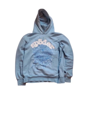Blå hoodie med spindelnätsmönster - Snygg ljusblå hoodie från Spyder med stor huva och coolt spindelnätsmönster framtill. Tryckt logga i vitt ovanför nätet och klassisk känguruficka. Perfekt för dig som gillar streetwear och vill sticka ut lite extra.