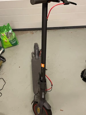 Svart elscooter Xiaomi Mi Electric - Säljer en svart elscooter från Xiaomi, modell Mi Electric Scooter. Scootern har röda detaljer på bromskabeln och reflexer på hjulen. Den har en bred ståplatta med halkskydd och ett smidigt styre med handbroms. Perfekt för att ta sig runt i stan.