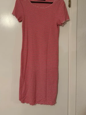 Randig röd och vit klänning BikBok - Superfin kortärmad klänning från BikBok i rött och vitt randigt mönster. Modellen är rak och kort, med stretchigt material och vågiga kanter vid ärmslut och nederkant. Perfekt för en avslappnad och trendig look.