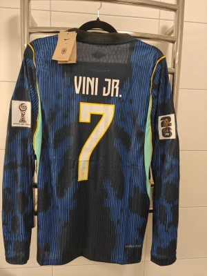 Brasilien Vini Jr. långärmad matchtröja spelar Version  - Spelar version, säljer enl långärmad Brasilien matchtröja från Nike med Vini Jr. och nummer 7 på ryggen. Tröjan är blå med svarta och gula detaljer, har FIFA och VM-märken på ärmarna samt CBF-logga på bröstet. Tillverkad i lätt funktionsmaterial (AEROSWIFT).
