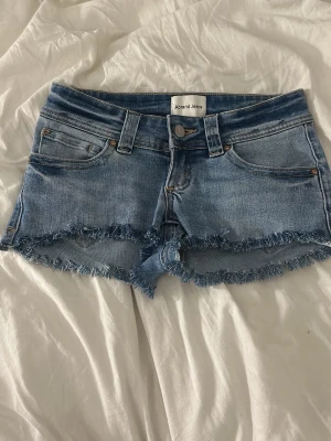 Blå jeansshorts med fransig kant - Säljer ett par ljusblå jeansshorts från Abrand Jeans med fransig kant nertill och klassisk femficksdesign. Shortsen har bälteshällor, knappgylf och en avslappnad passform. Perfekta för varma dagar och enkel att matcha med allt, Egen gjorda.