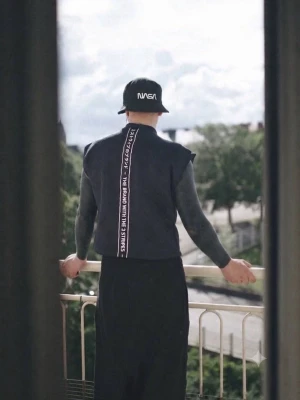 Svart quiltad väst med textdetalj - Säljer en svart quiltad väst med markerade axlar och en vertikal textdetalj på ryggen där det står 'THE BRAND WITH THE 3 STRIPES' samt japanska tecken. Västen har en modern, boxig passform och är tillverkad i ett vadderat material.