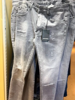 Grå slitna jeans från Dsquared2 - Säljer ett par grå jeans från Dsquared2 med slitningar och distressed detaljer. Jeansen har fem fickor, bälteshällor och en smal passform. Snyggt tvättade för en trendig look och med Dsquared2-logga på framsidan.