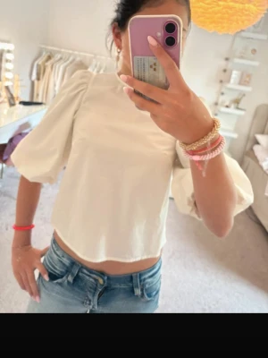 Vit blus med puffärmar - Säljer en söt vit blus med puffiga trekvartsärmar och rak passform. Toppen är croppad och har en enkel, stilren design som passar perfekt till jeans eller kjol. Materialet känns lätt och luftigt, perfekt för varmare dagar.