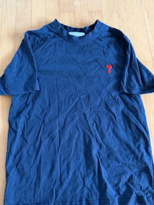 Ami Paris  - Snygg marinblå t-shirt i bomull med korta ärmar och ett broderat rött hjärta med bokstaven A på bröstet. Enkel och stilren design som passar perfekt till jeans eller shorts.