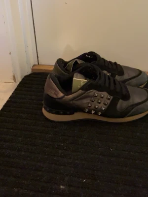 Svarta sneakers med nitar - Snygga svarta sneakers med metallic-detaljer och silverfärgade nitar på sidorna. Skorna har svarta snören, svart sula med beige kant och en cool, urban look. Perfekta för dig som vill sticka ut med din stil.