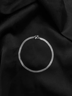 Silver kedjearmband - Stilrent armband i silverfärg med tunn, platt kedja och enkel krokspänne. Armbandet har en minimalistisk design och passar perfekt för dig som gillar diskreta accessoarer. Materialet ser ut att vara metall med en blank finish.
