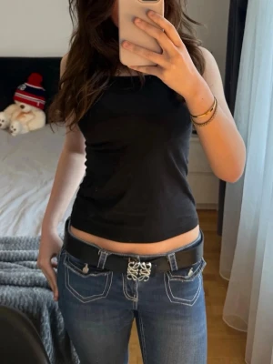 Vändbart bälte  - Säljer ett snyggt vändbart bälte, i färgen svart och orange, med ett unikt och dekorativt metallspänne framtill. Bältet har klassisk form och passar perfekt till jeans eller kjol. Materialet är slätt och ger en stilren look.