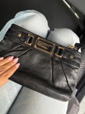 Svart kuvertväska Marc by Marc Jacobs - Väskan har guldfärgade metalldetaljer och en dekorativ metallbricka framtill med märkets logga. Stilren design med veckade detaljer och dragkedja upptill. Säljer denna otroligt fina vintage Marc Jacobs clutch. Den är helt perfekt till vardag och utekvällar. Får plats med mobil plånbok mm då den är rymlig. Säljs inte längre! 🤗 inga defekter