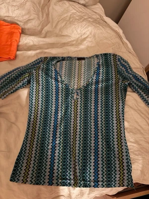 Mönstrad långärmad topp med v-ringning - Säljer denna superfina vintage/second hand-top från Just Cavalli. Den har ett klassiskt blått geometriskt mönster i olika nyanser av blått, turkost, grått och olivgrönt samt en figurnära passform med stretch som sitter väldigt snyggt.  Toppen är i fint använt skick, men har ett litet hål på högra axeln (se bild), vilket inte påverkar användningen och går att laga om man önskar.  Detaljer:  * Äkta Just Cavalli * Långärmad * Stretchigt material * Figurnära passform * Y2K/vintage-look