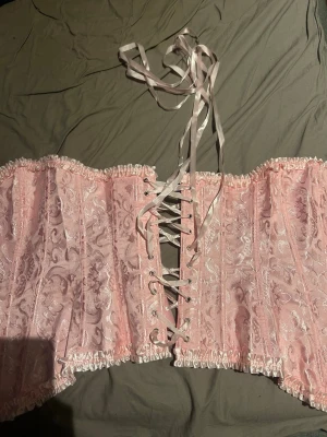 Rosa korsett - Säljer en söt rosa korsett då jag beställde fel, har bara testat den, med kläder på såklart. Köpte den på shein för 150kr. Den har ett vackert blommigt mönster och snörning i ryggen. Korsetten har dekorativa spetskanter upptill och nedtill.😊 kom gärna me prisföslag om nån är onöjd