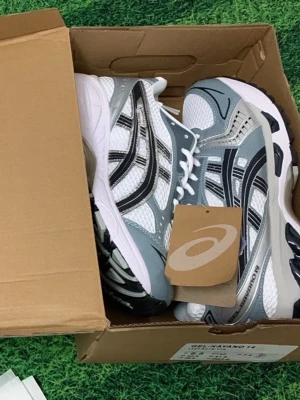 Asics Gel-Kayano 14 vita/grå sneakers - Snygga ljus blåa Asics Gel-Kayano 14 sneakers med vitt grått och svarta detaljer. Ovandelen är i mesh och syntet för bra andningsförmåga och komfort. Klassisk sportig siluett med vita snören och robust sula. Perfekta för dig som gillar retrostil och streetwear.