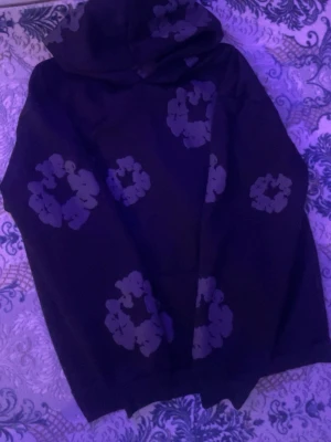 Svart hoodie med blommönster - Säljer en svart hoodie med stora blommönster i grått. Hoodien har lång ärm och en klassisk huva. Perfekt för dig som gillar en chill och unik stil. Passar till både jeans och mjukisbyxor.