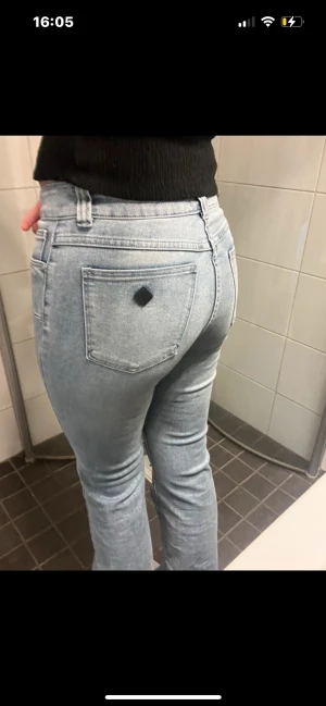 Ljusblå raka jeans med fickdetalj - Säljer ett par ljusblå jeans med rak passform och klassisk femficksdesign. Jeansen har en svart fyrkantig detalj på ena bakfickan och är tillverkade i denim med lätt tvättad look. Perfekta för en avslappnad och trendig stil.