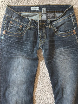 Low waist bootcutjeans - Snygga mörkblå bootcut jeans från Clockhouse med slitningar och kontrastsömmar. Klassisk femficksmodell och låg midja. Jeansen har kopparfärgade nitar och är tillverkade i bomull med lite stretch för skön passform. Lite små i storleken