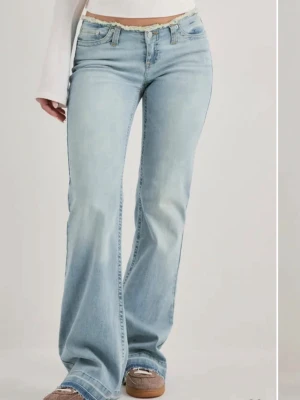Ljusblå bootcut jeans med låg midja - Säljer ett par ljusblå bootcut jeans med låg midja och rå kant upptill. Jeansen har klassisk femficksdesign och är tillverkade i denim med lätt tvättad look. Perfekta för en avslappnad och trendig stil.lite smutsigt nertill men hår bort i tvätten 