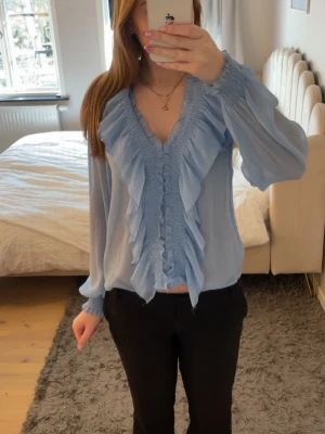 Ljusblå volangblus med v-ringning från Zara  - Supersöt ljusblå blus med v-ringning och volangdetaljer framtill. Blusen är från Zara och är i storlek xs