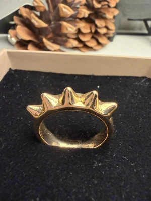 Guldig ring med pyramidformade detaljer - Cool ring i guldfärgad metall med fem pyramidformade spetsar som ger en edgy och unik look. Ringen har en blank finish och passar perfekt för dig som vill sticka ut med dina accessoarer. Snygg att bära ensam eller att matcha med andra ringar.