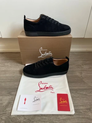 Christian Louboutin skor svart - Stilrena svarta sneakers från Christian Louboutin i mocka med matchande svarta skosnören och diskret logga på insidan. Låg modell med klassisk siluett och svart sula. Perfekta för dig som gillar exklusiv och tidlös design.